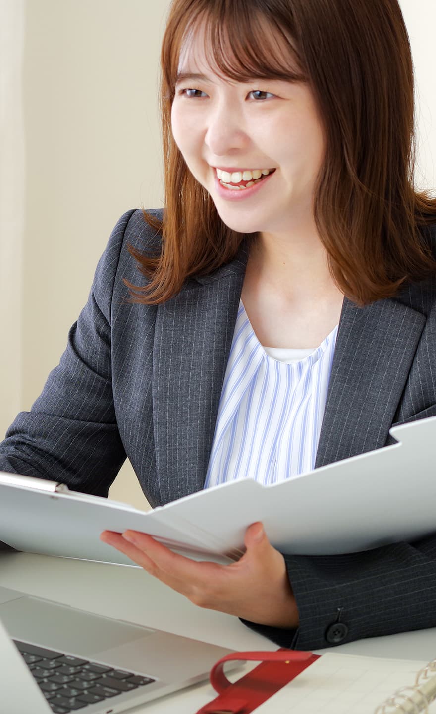 手にバインダーを持ったスーツ姿の女性が笑顔で話をしている様子